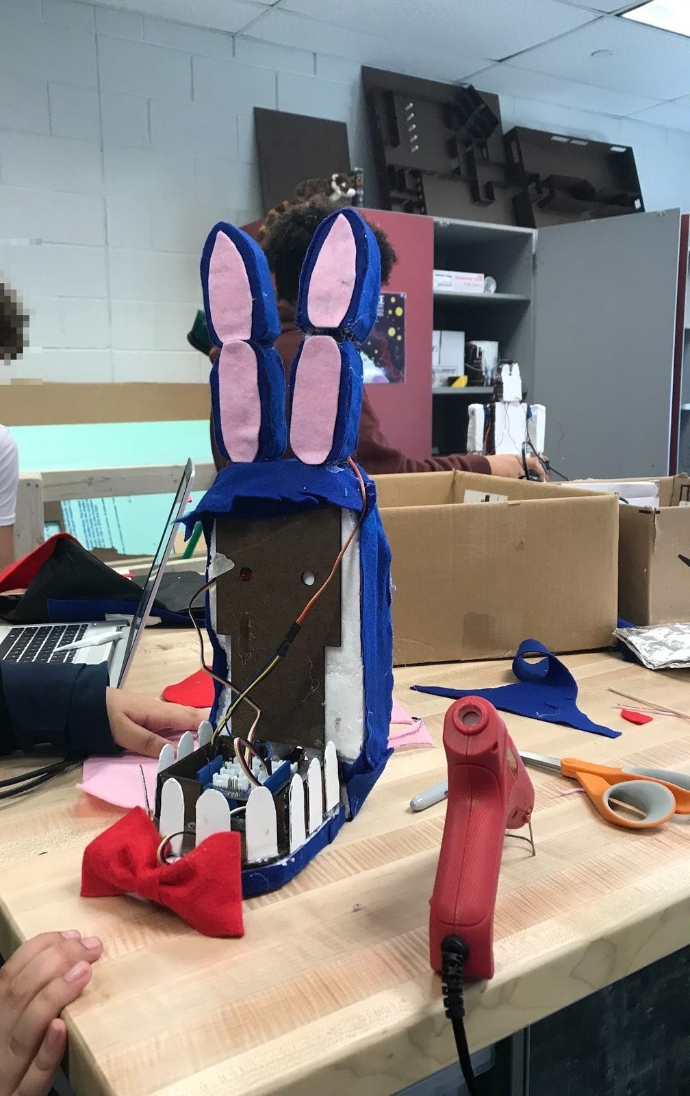 Animatronic bunny head in progress with felt ears, a bow tie, and exposed electronics
