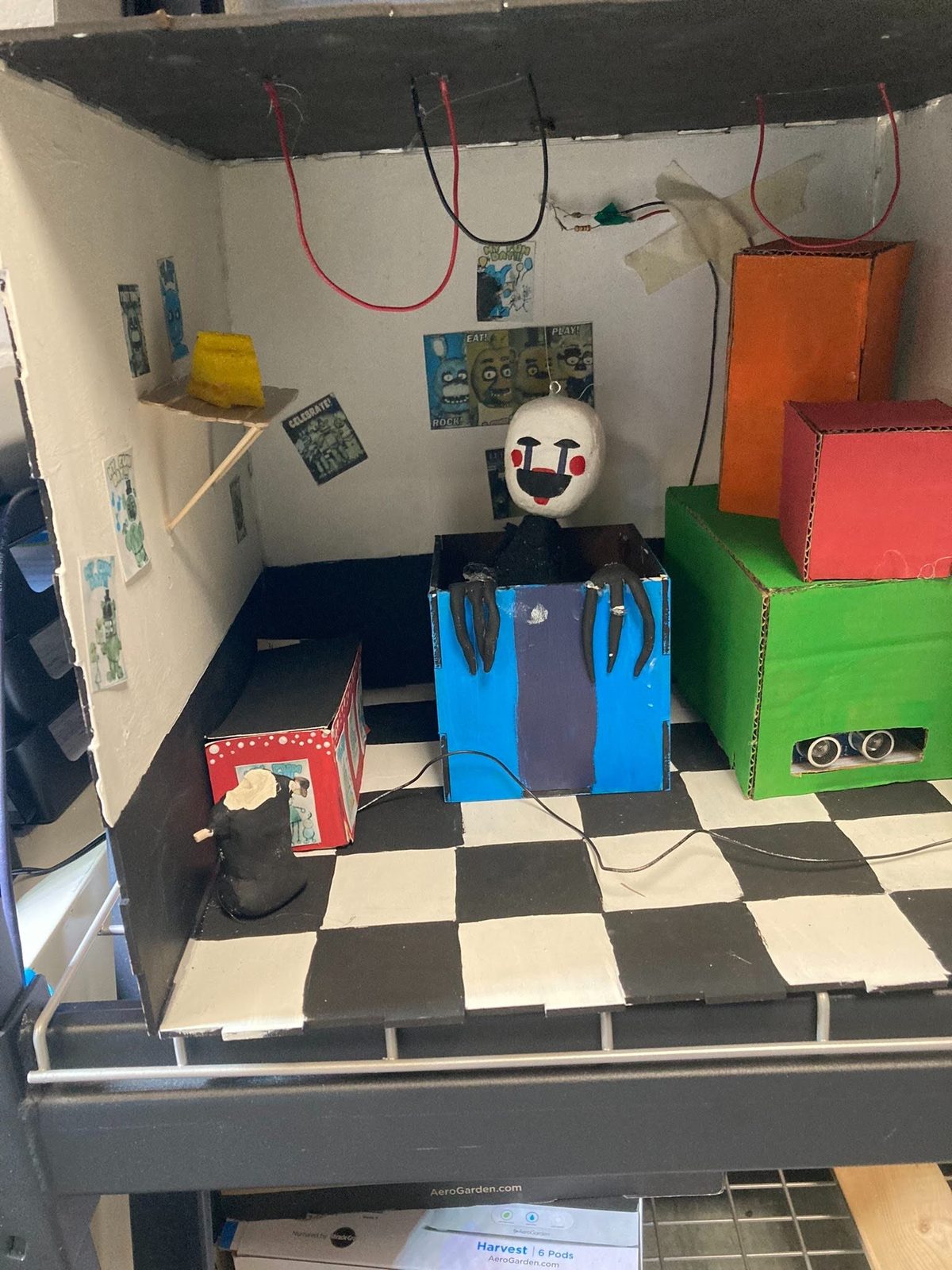 Puppet-style animatronic head with a painted mask and clawed hands emerging from a decorated box