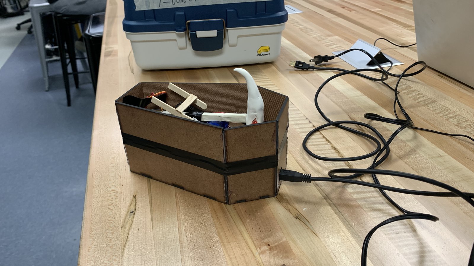 Laser-cut wooden project box with servo parts and wiring inside, next to a tackle box