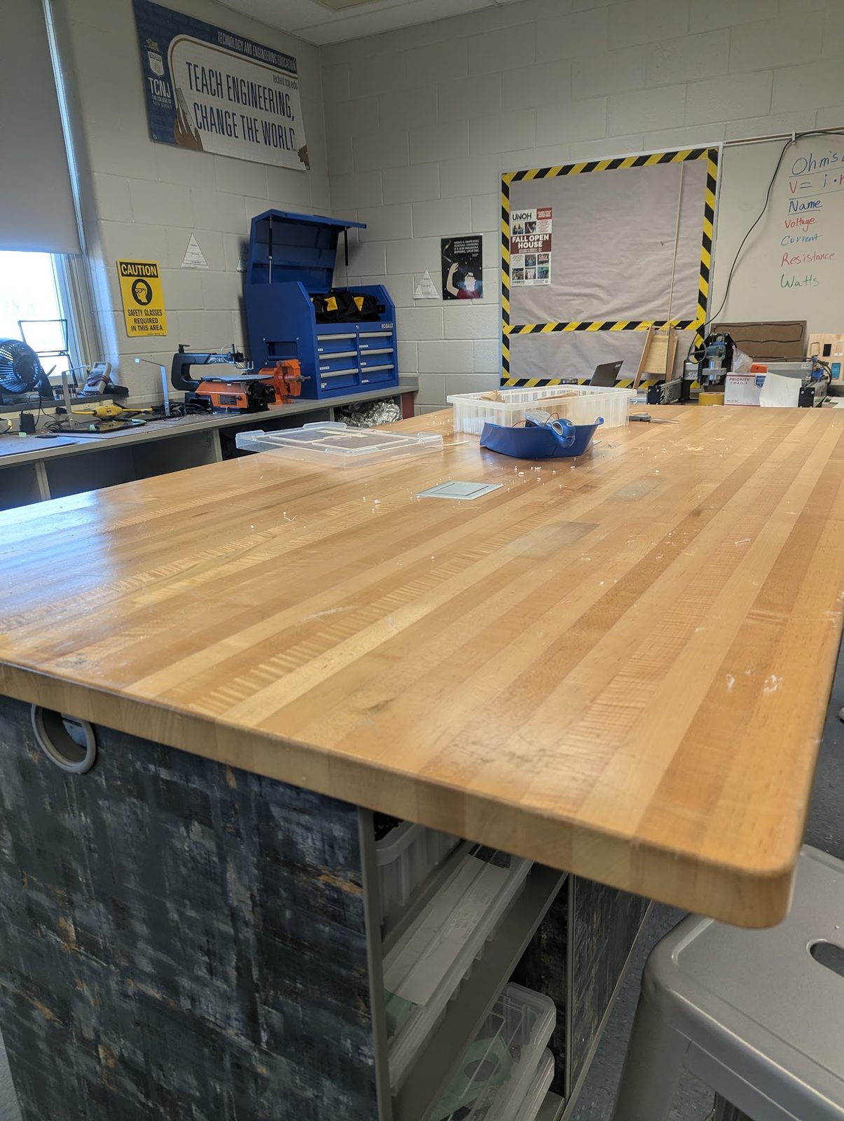 After: close-up of a butcher-block pod desk with an Ohm's Law lesson on the whiteboard behind it