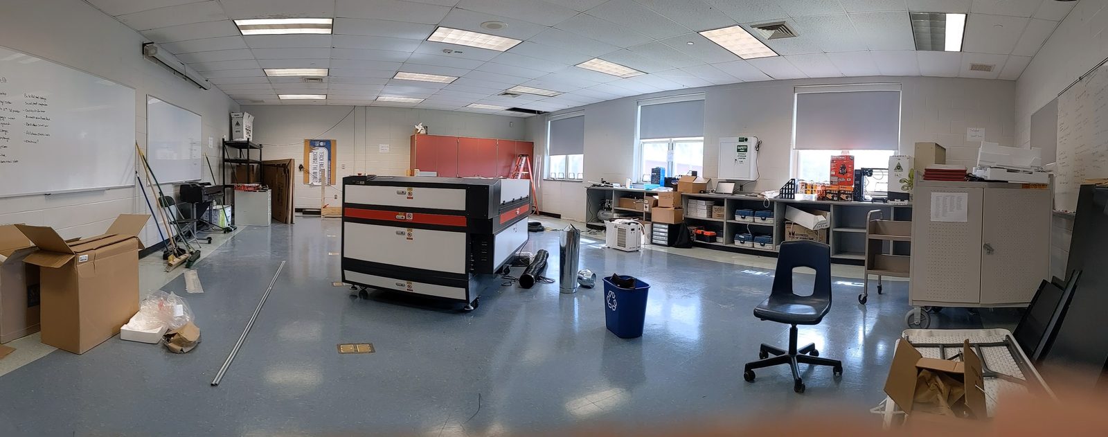 Wide panoramic view of the lab mid-setup, with the new laser cutter in place and moving boxes still scattered around