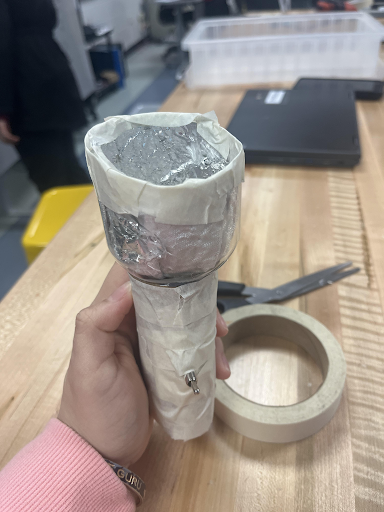 Hand holding a flashlight prototype made from a cup wrapped in foil and tape