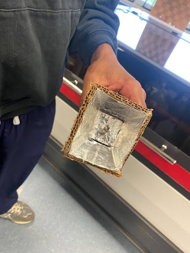 Student holding a cardboard and foil reflector-style flashlight housing