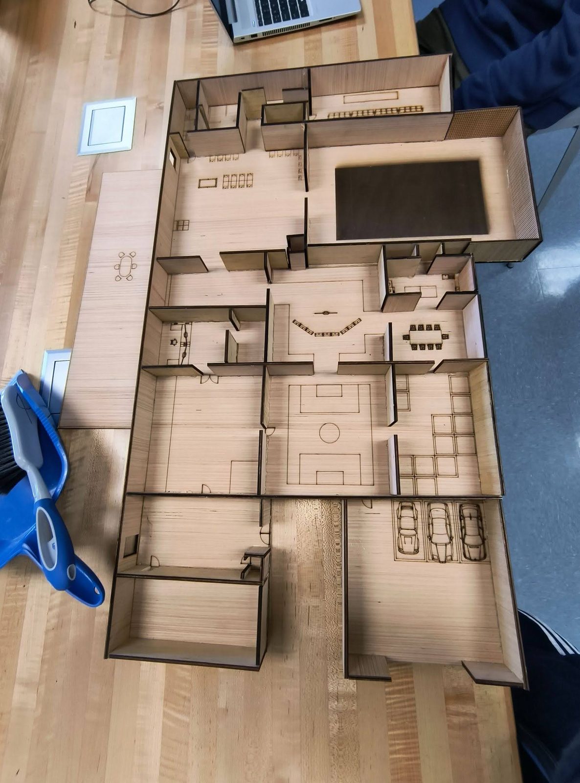 Overhead view of a laser-cut wood house model with etched furniture, a pool, and a three-car garage