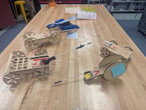 Three laser-cut mousetrap cars lined up on a butcher-block pod desk