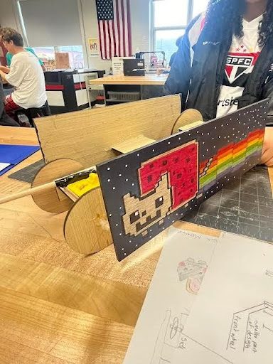 Mousetrap car painted with a Nyan Cat design, held up in the classroom
