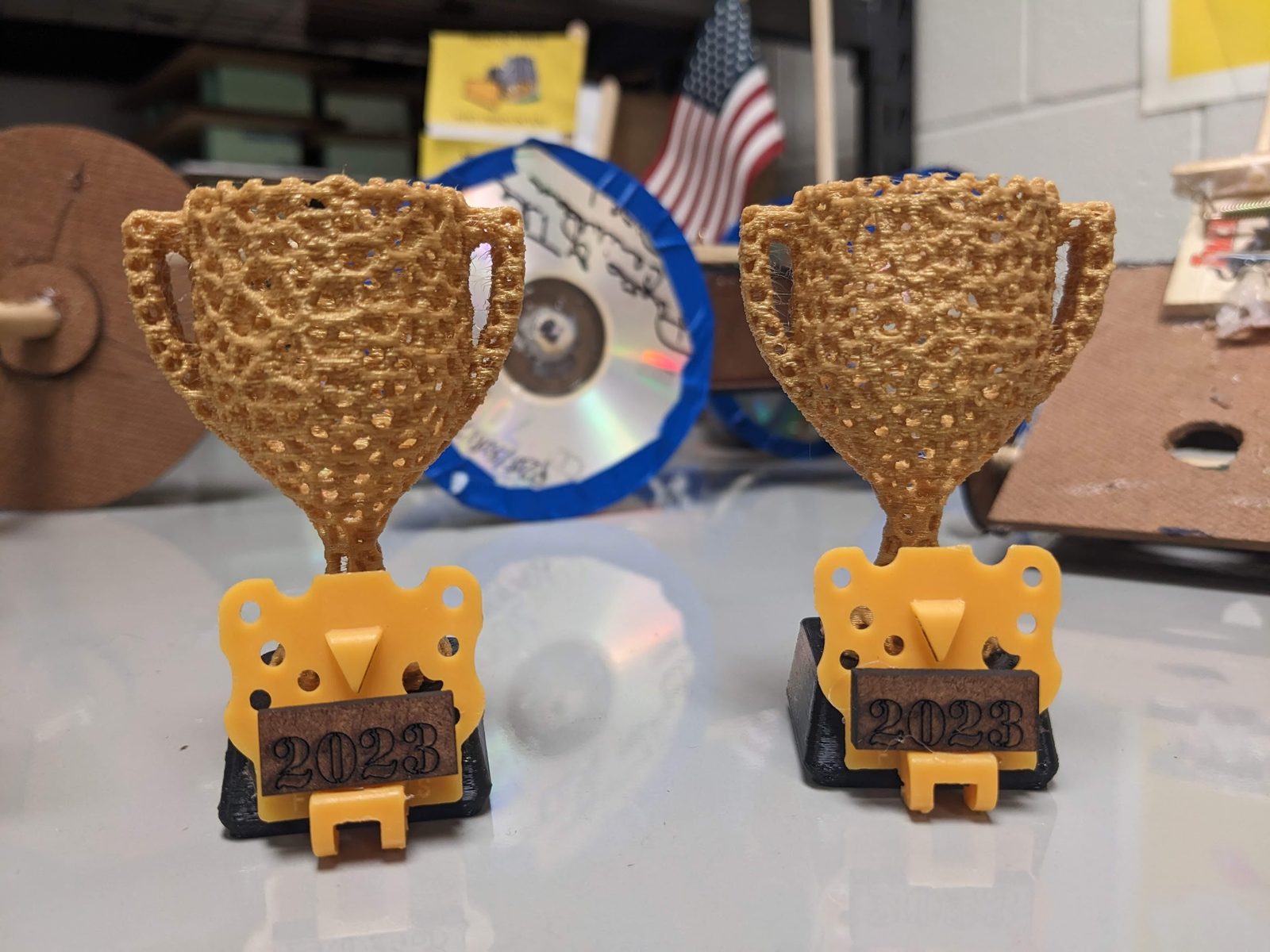 Two 3D-printed trophy cups on laser-cut mousetrap car chassis stands, engraved 2023