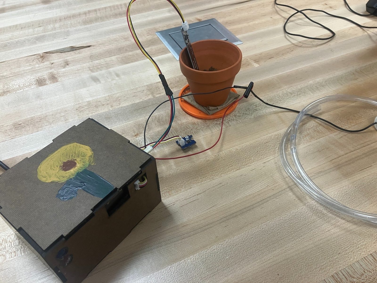 Finished plant babysitter box hand-painted with a sunflower, wired to a moisture sensor in a potted plant