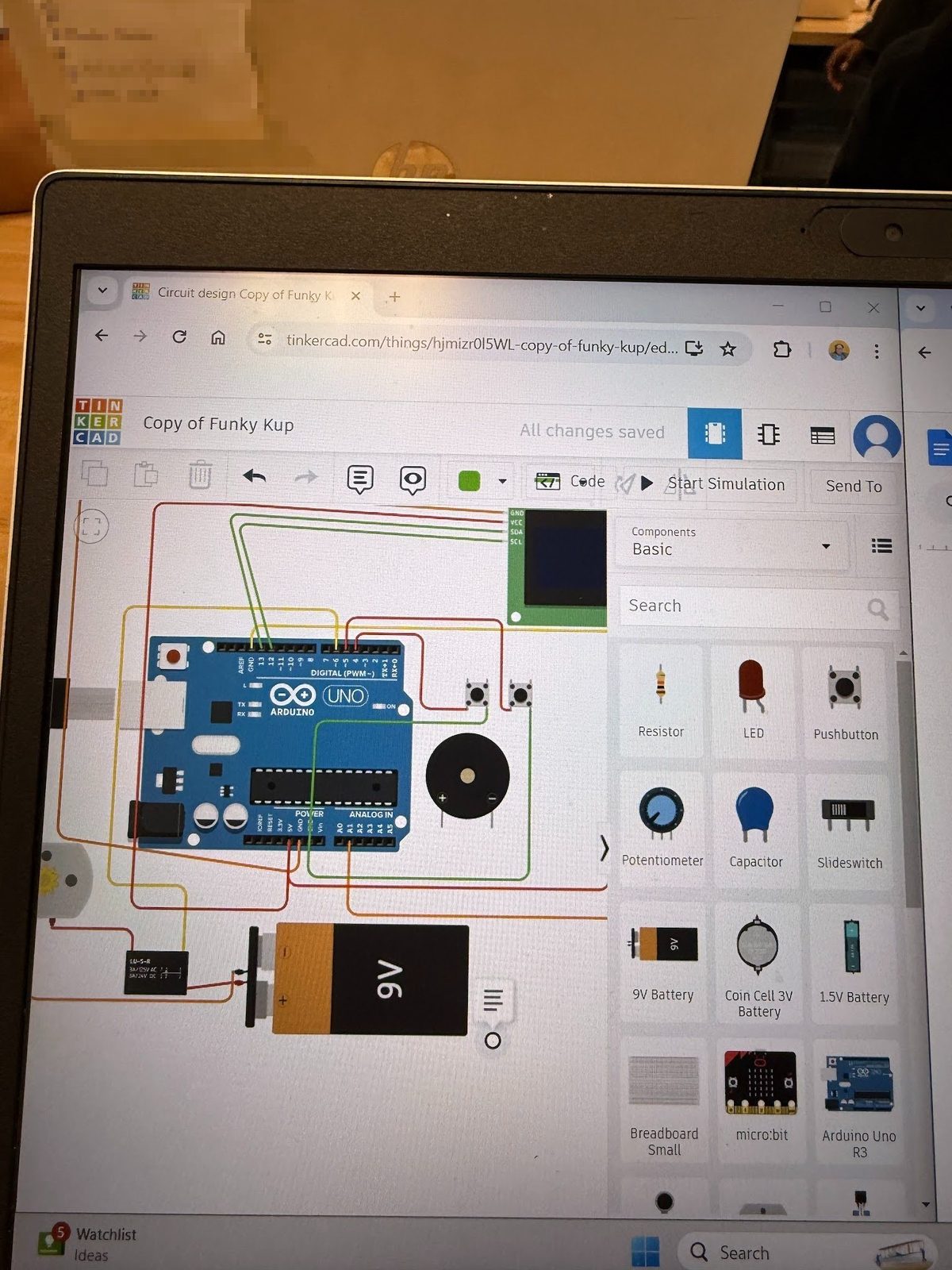 Laptop screen showing an early TinkerCad Arduino circuit prototype with a buzzer, buttons, and OLED display