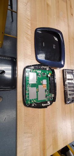 A Wi-Fi router opened up, showing the internal circuit board and antenna wires next to the casing