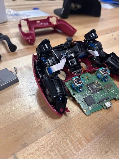 Disassembled game controller with joysticks, triggers, battery, and circuit board separated on a workbench