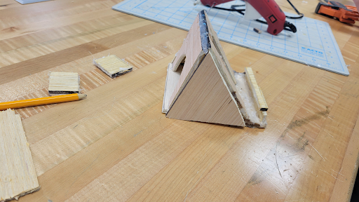 Triangular A-frame wooden phone stand on a workbench next to a hot glue gun
