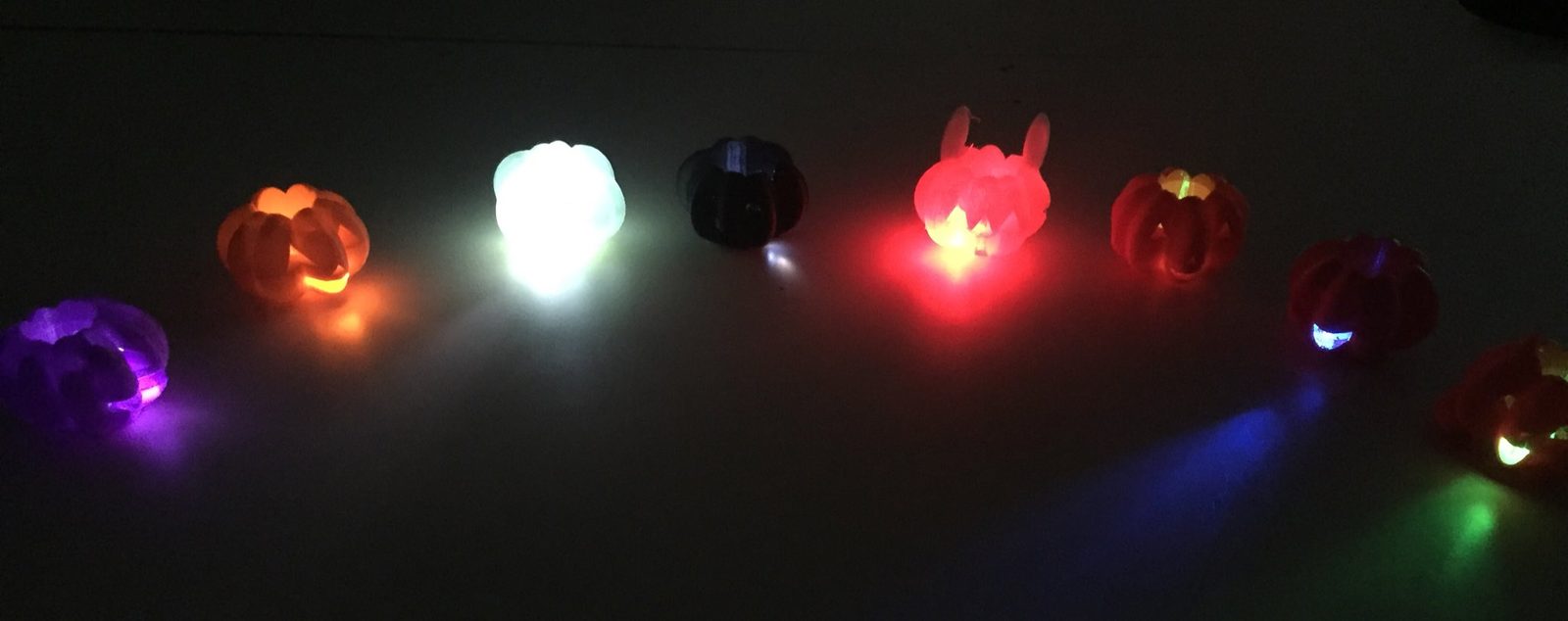 Row of glowing 3D printed jack-o-lantern lanterns in different colors