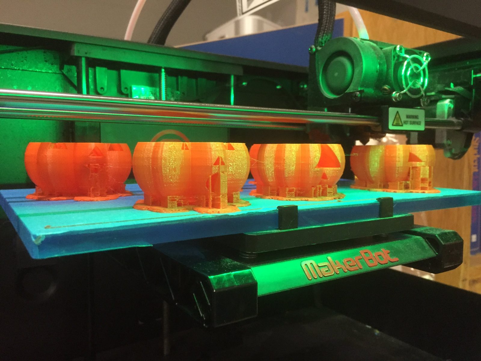 Four jack-o-lantern lanterns fresh off the 3D printer bed, still warm from the MakerBot
