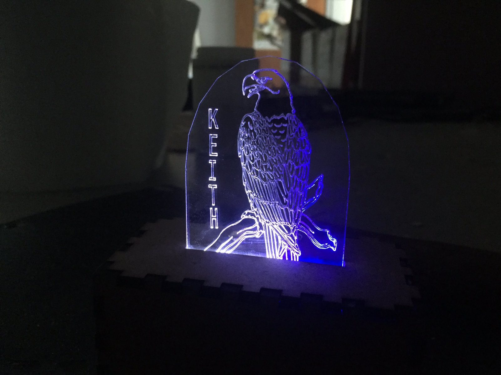 Edge-lit acrylic panel engraved with a perched eagle and the name Keith, glowing blue, mounted in a laser-cut wooden base