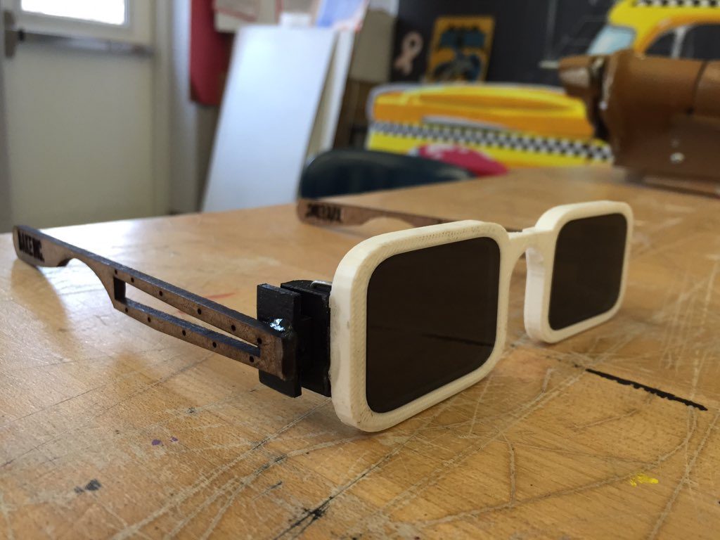 Finished sunglasses with 3D printed white frame, tinted lenses, and laser-cut wooden arms, angled on a workbench