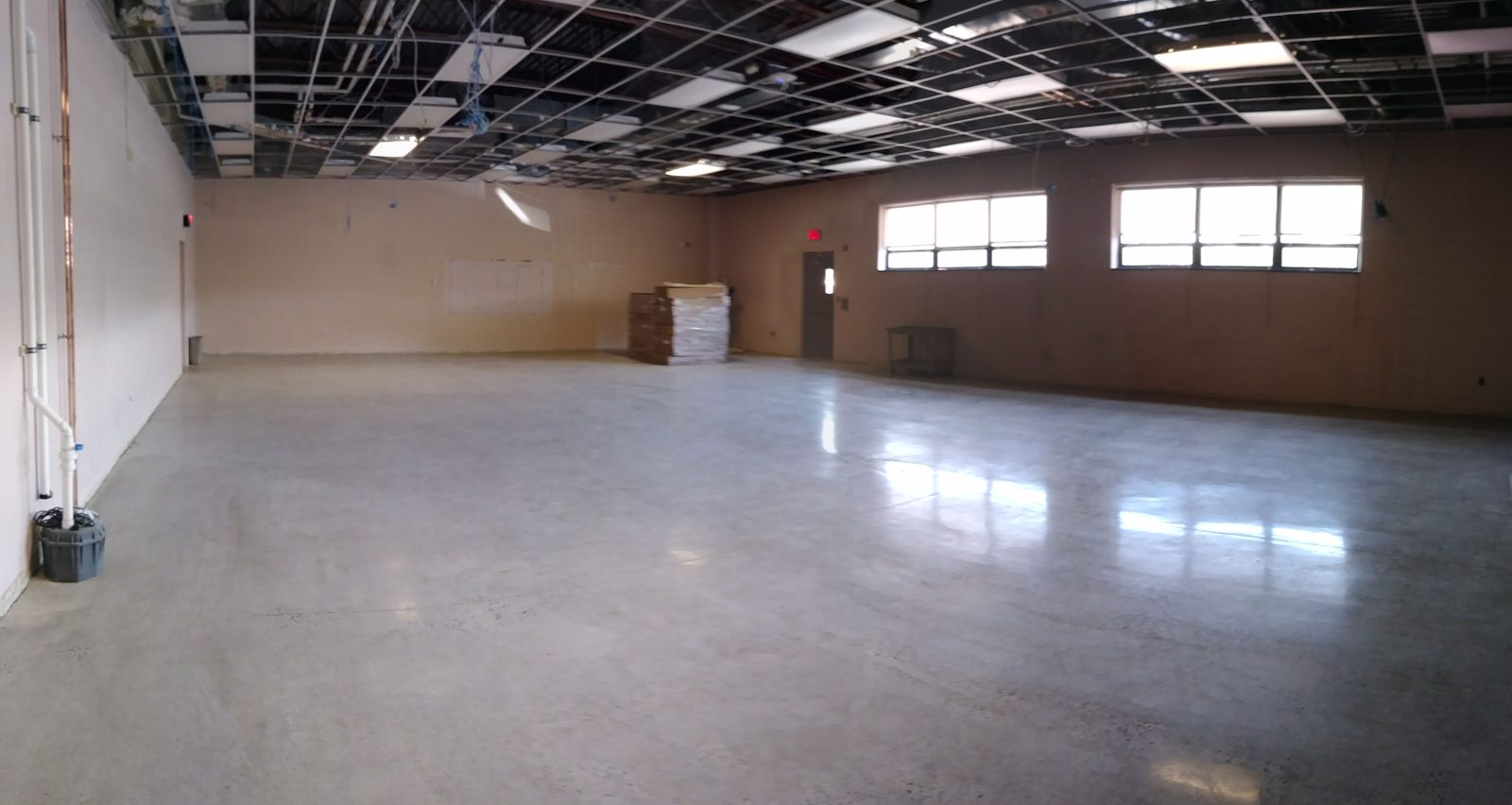 Empty raw classroom space with exposed ceiling grid and bare concrete floor, before the lab build-out