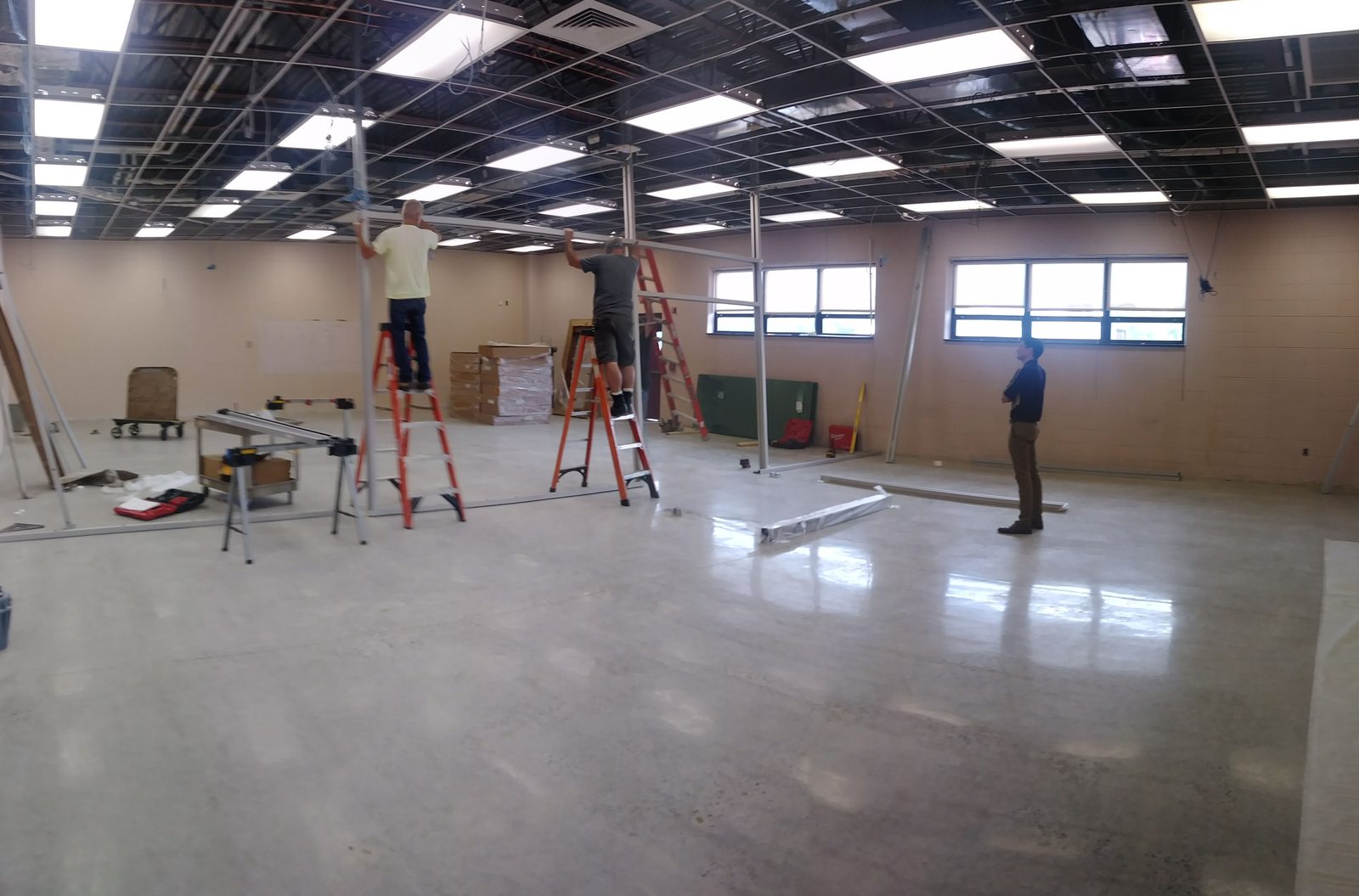Workers on ladders installing ceiling framework in the empty lab space during construction