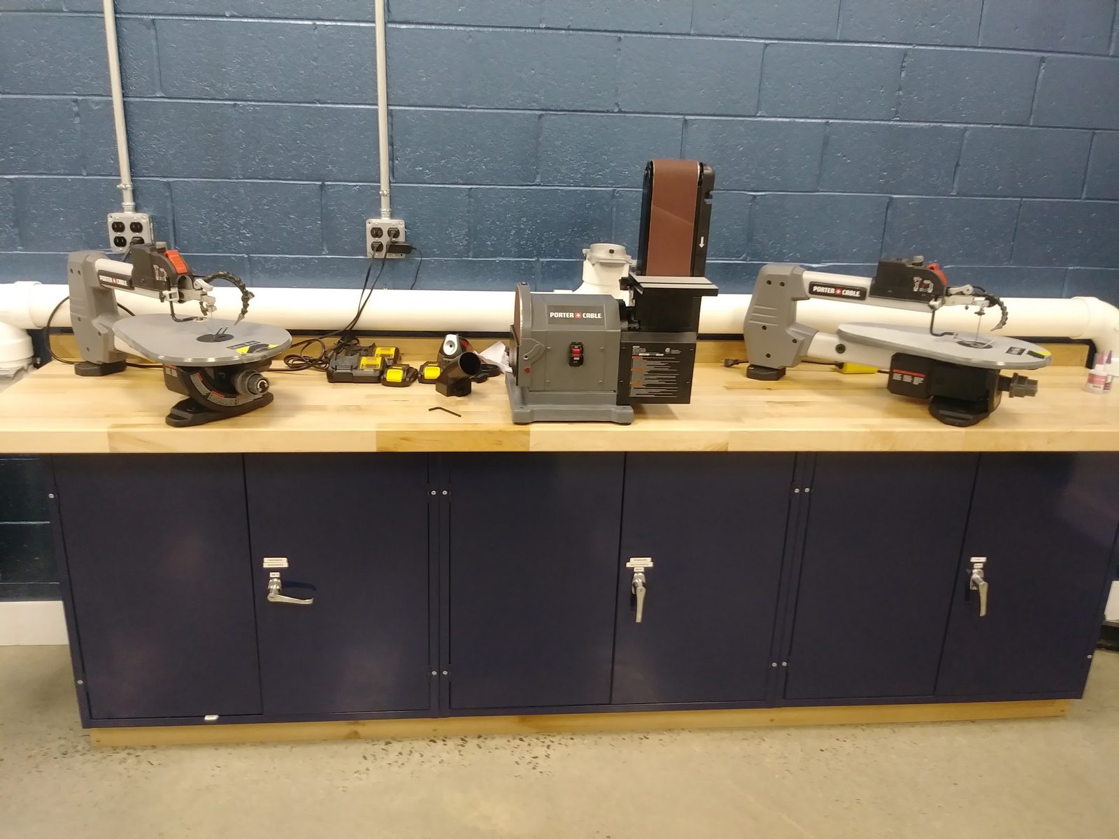 Workbench with two scroll saws, a disc/belt sander, and battery packs for cordless tools