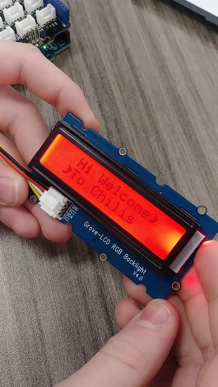 Close-up of a Grove LCD RGB backlight display wired to a sensor board, showing a custom welcome message
