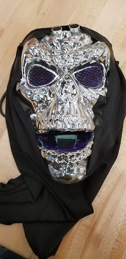 Chrome skeleton mask animatronic with glowing LED eyes, wrapped in a black hood