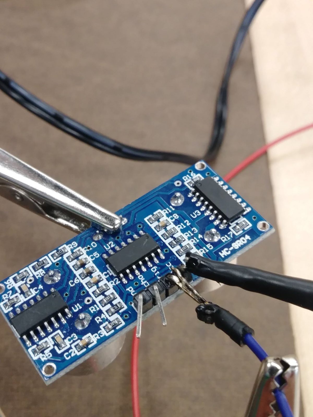 Close-up of an ultrasonic sensor circuit board wired up with alligator clip test leads