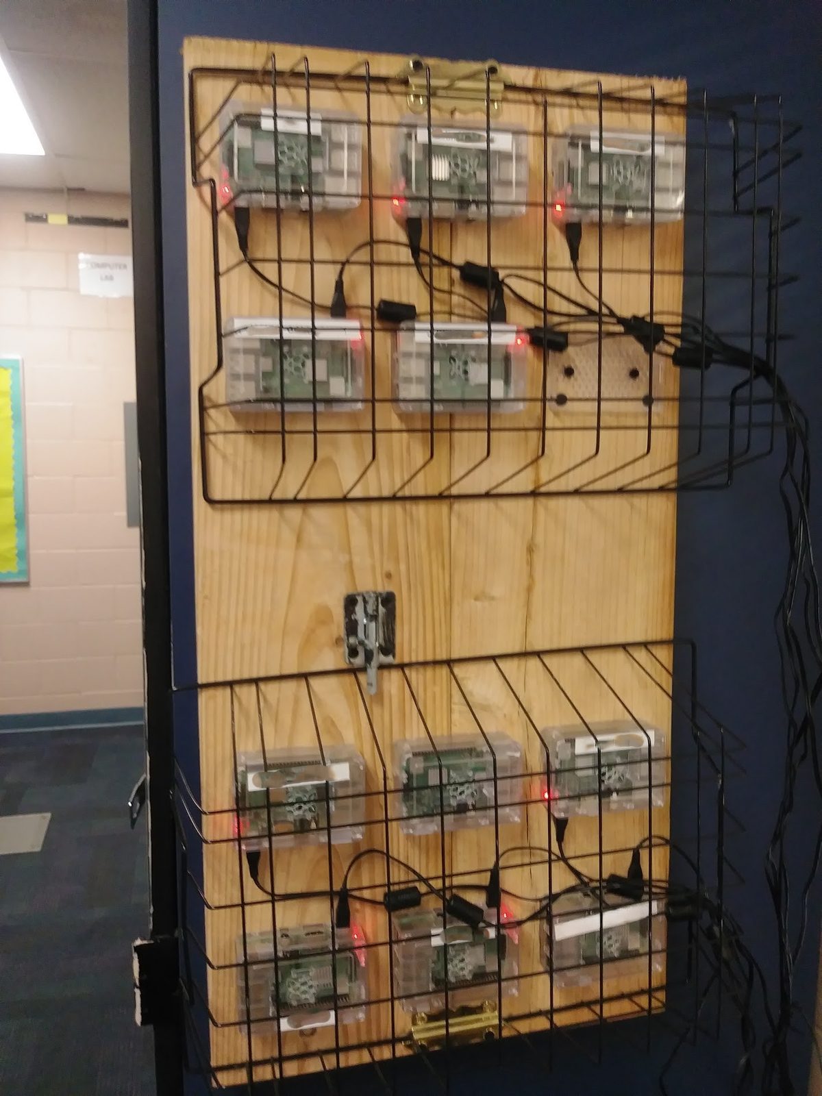 Class set of Raspberry Pis mounted in wire racks on a wooden board, each powered on with an active LED