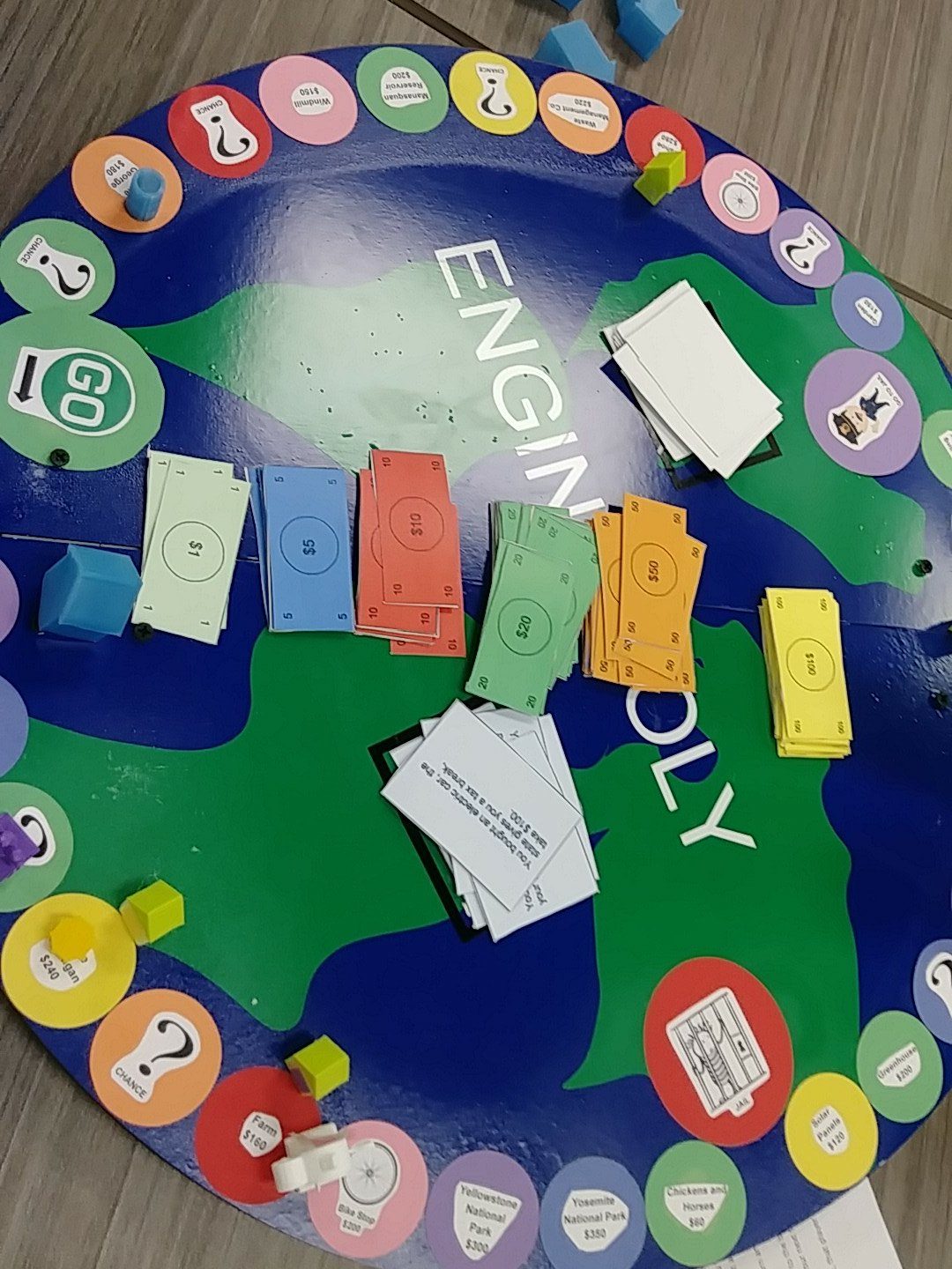 Student-designed Engin-opoly board game with a sustainability theme, featuring windmills, solar panels, and waste management spaces