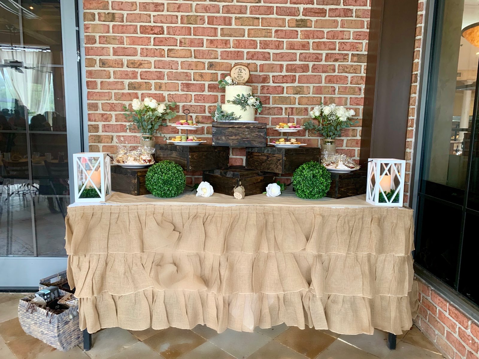Finished centerpiece boxes stacked as dessert table risers at a real catering event, with a cake, macarons, and flowers