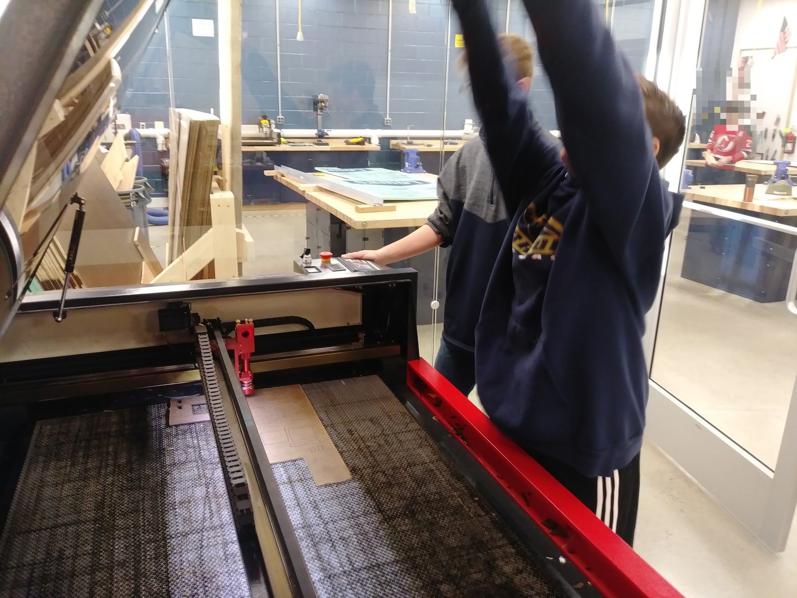 Students at the large-format laser cutter mid-cut on a mousetrap car part