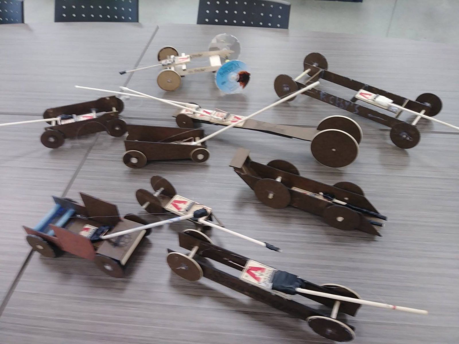 A whole class set of finished mousetrap cars with wheels, chassis, and lever arms lined up on a table