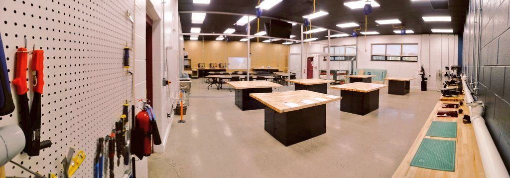 Finished engineering lab with a wall of hand tools, black workbenches with butcher-block tops, and large windows