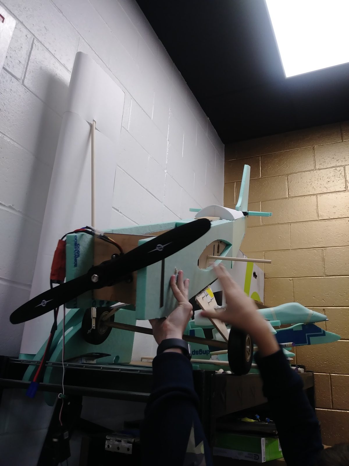 Foam RC plane fuselage with propeller and motor mount, held up in the classroom during assembly