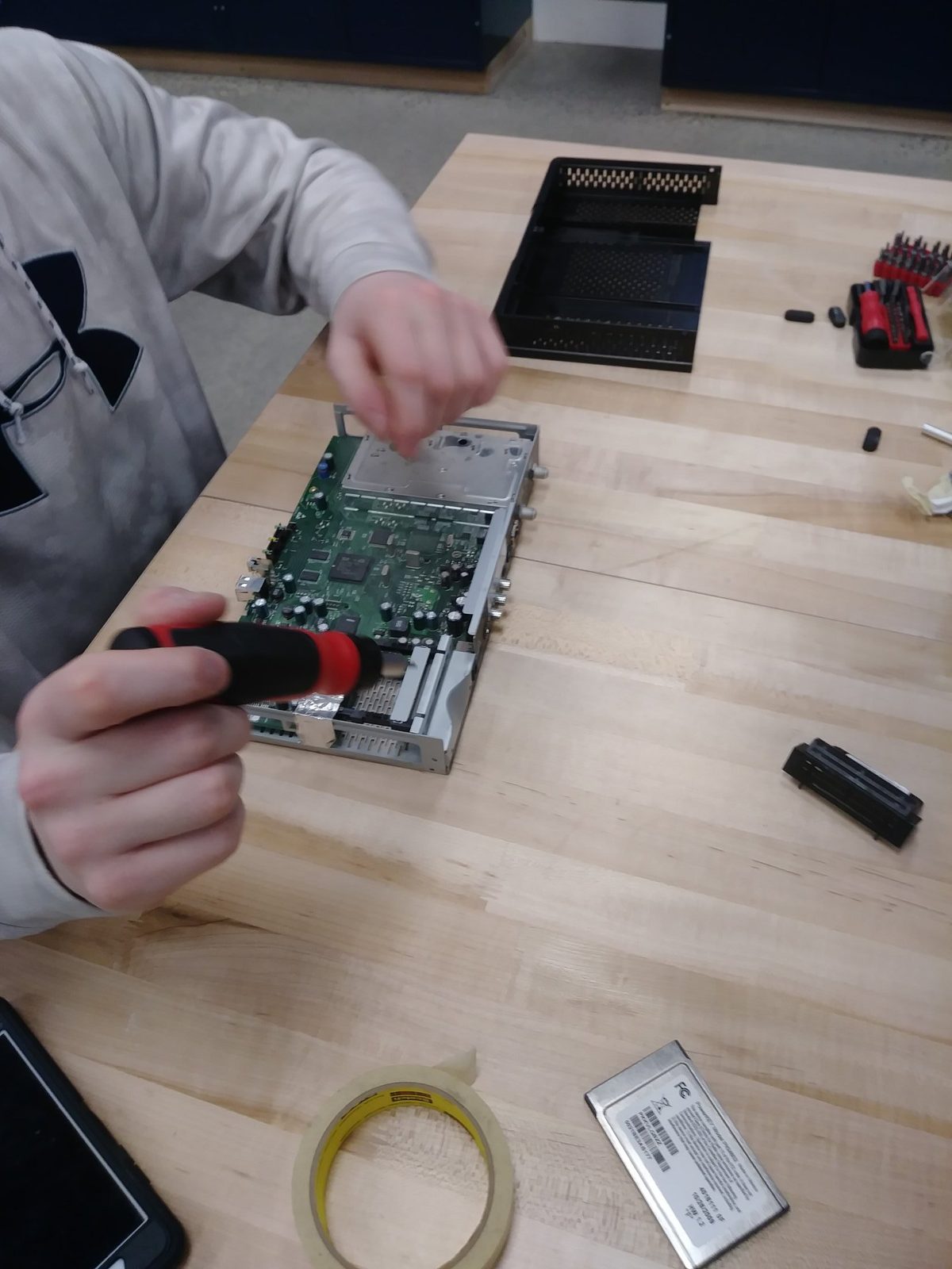 Student disassembling a set-top box circuit board with a screwdriver