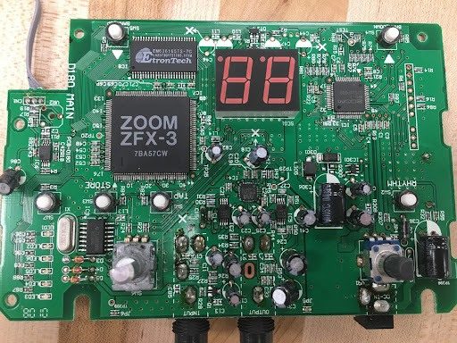 Close-up of a guitar effects pedal circuit board with a labeled chip and seven-segment display