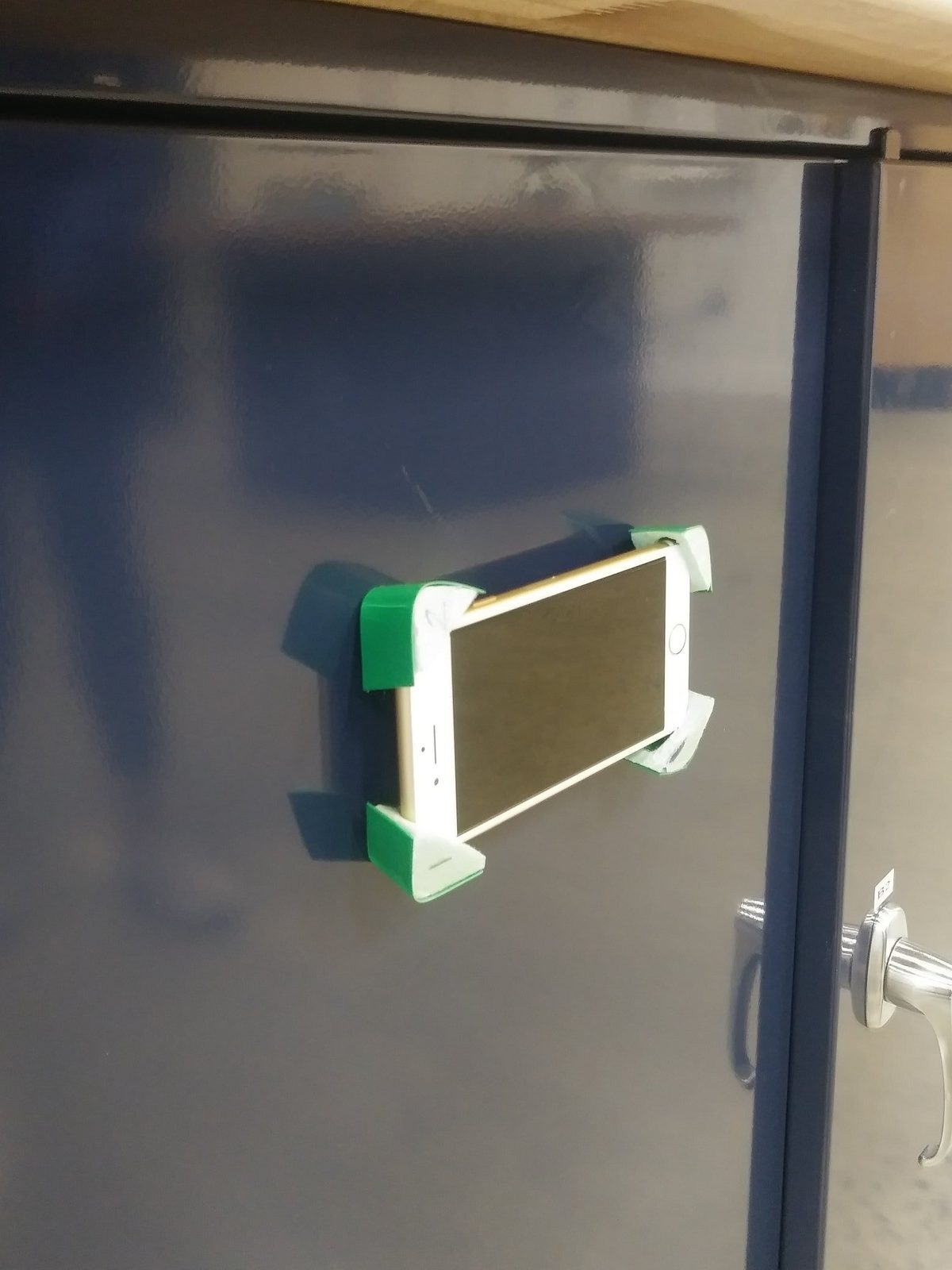 A 3D-printed magnetic phone mount holding a phone against a metal locker door