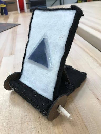 A black felt-covered phone stand with wooden wheel accents and a triangular magnetic mount piece