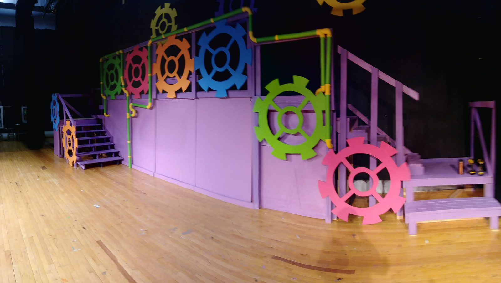 Empty stage set of a colorful gear-covered wall and staircase, built for Willy Wonka