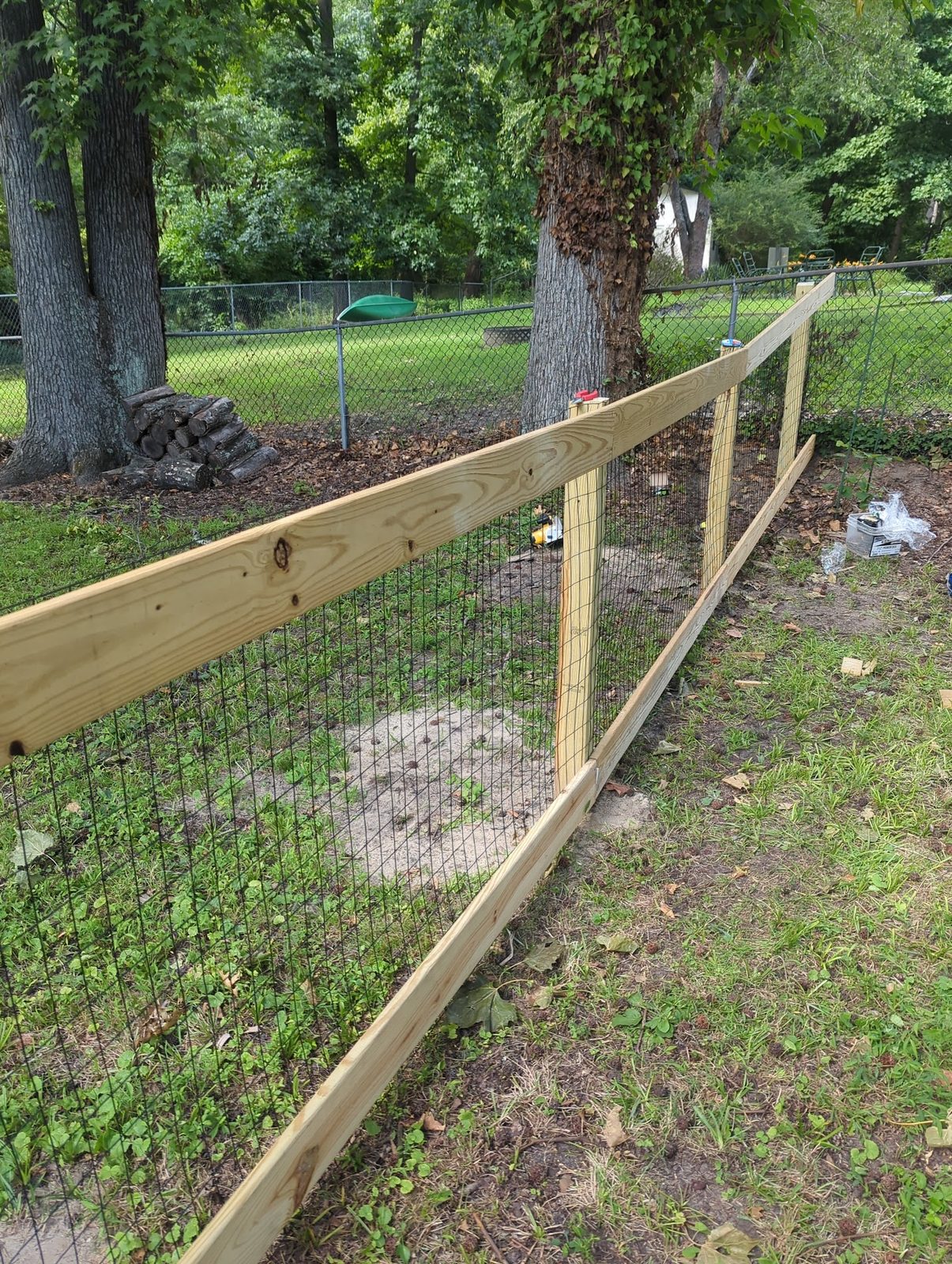 New wood-framed wire fence section under the trees