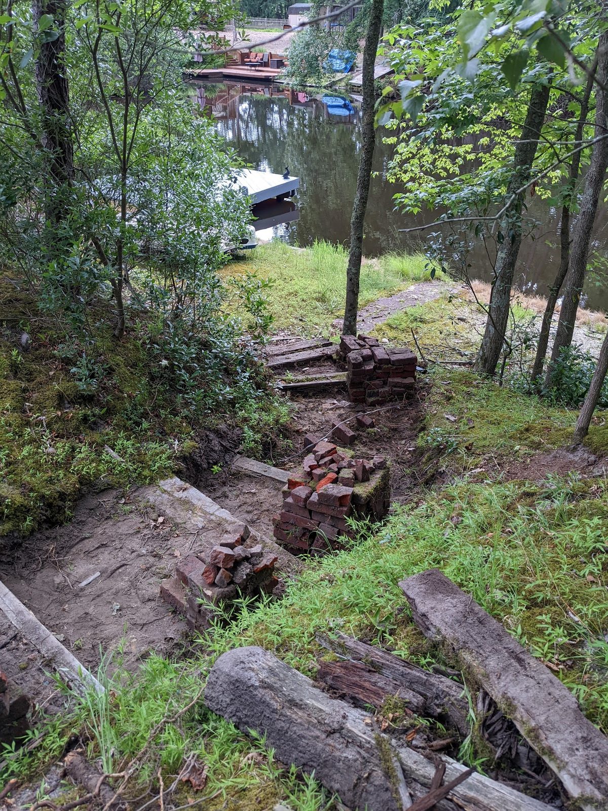 View down the client's wooded slope toward the creek with materials staged