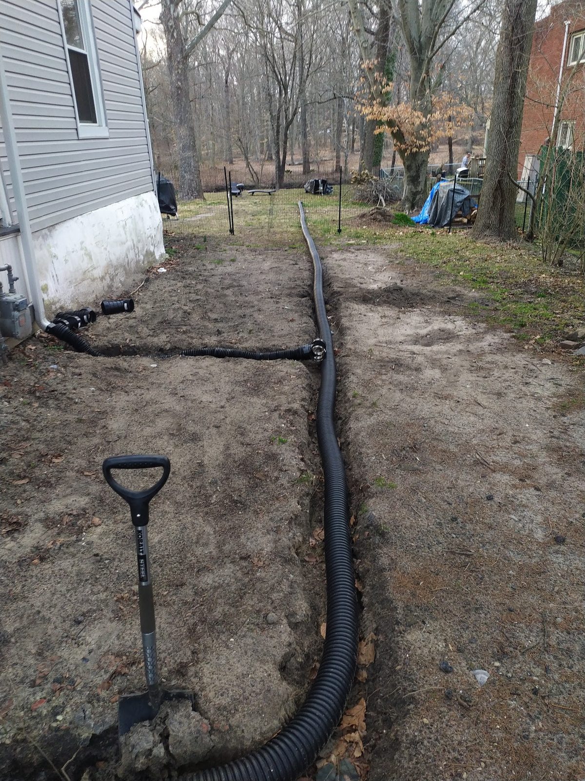 Shovel next to a drainage pipe being laid in the trench